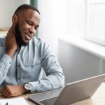 man sitting at table looking at laptop experiencing neck pain