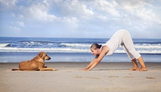 young woman doing downward dog yoga on beach