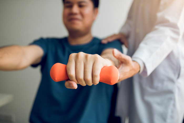 physical therapist assists patient with hand weights for healing